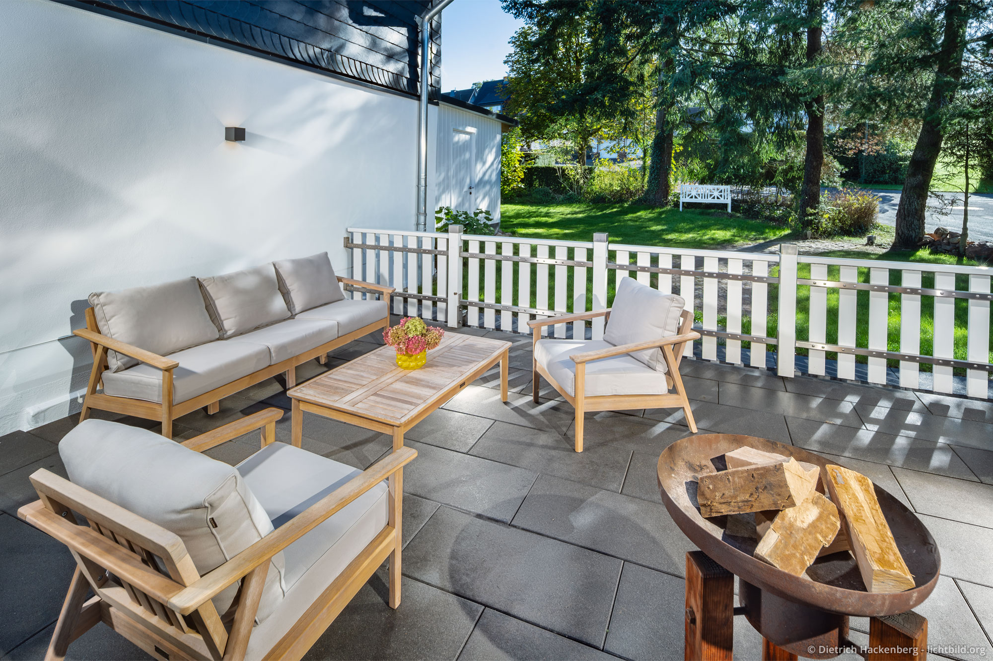 Terrasse in der Morgensonne mit Lounge und Feuerschale. Der Zaun ist komplett geschlossen.
