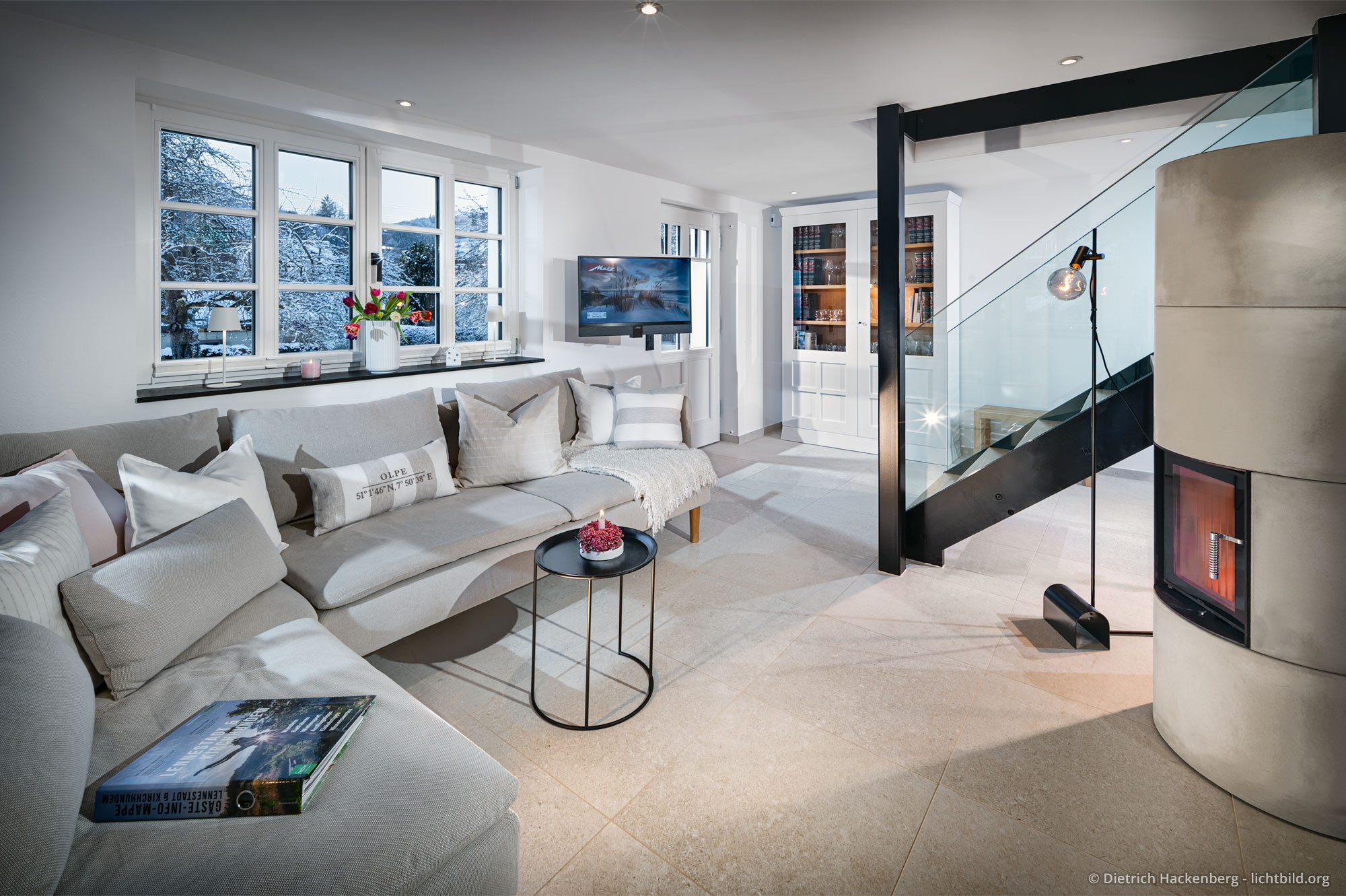 Sofaecke mit Fensterblick auf Schneelandschaft, Speicherofen und Treppenaufgang mit gläsernem Geländer. Ferienwohnung im Fachwerkhaus Eiben, Kirchhundem-Benolpe
