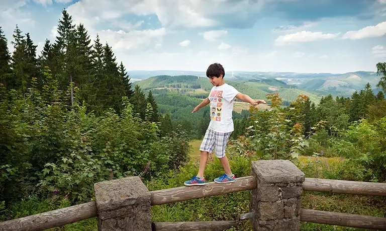 Junge balanciert auf einem Zaun vor der Aussicht von der Hohen Bracht